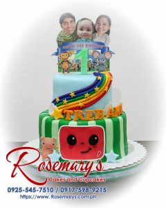 Delicious 2 layer Coco Melon themed cake in blue and green, featuring rainbow accents. Order from Rosemary's Cakes: 0925-545-7510.