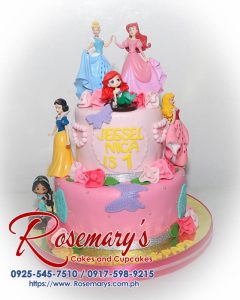Two-tier pink Disney Princess themed cake adorned with edible glitter and figurines of Ariel, Cinderella, Jasmin, Sleeping Beauty, and Snow White. Rosemary's Cakes | 0917-598-9215