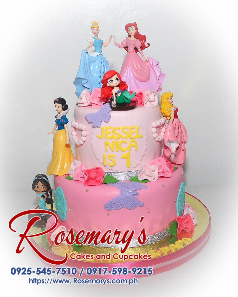 Two-tier pink Disney Princess themed cake adorned with edible glitter and figurines of Ariel, Cinderella, Jasmin, Sleeping Beauty, and Snow White. Rosemary's Cakes | 0917-598-9215